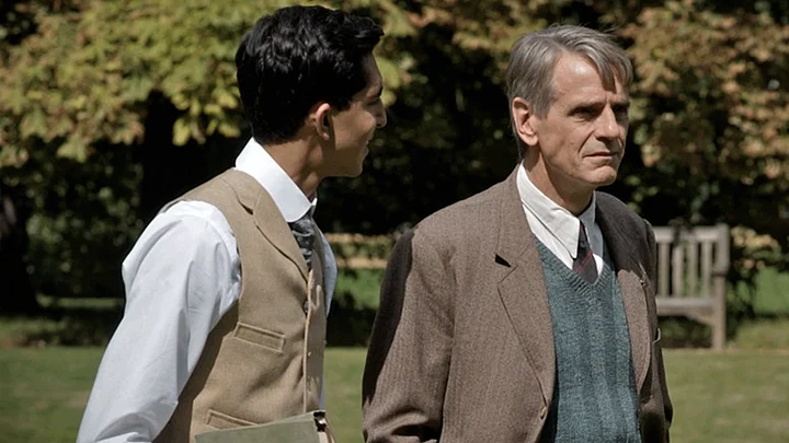 Two men in period dress standing outdoors beneath trees